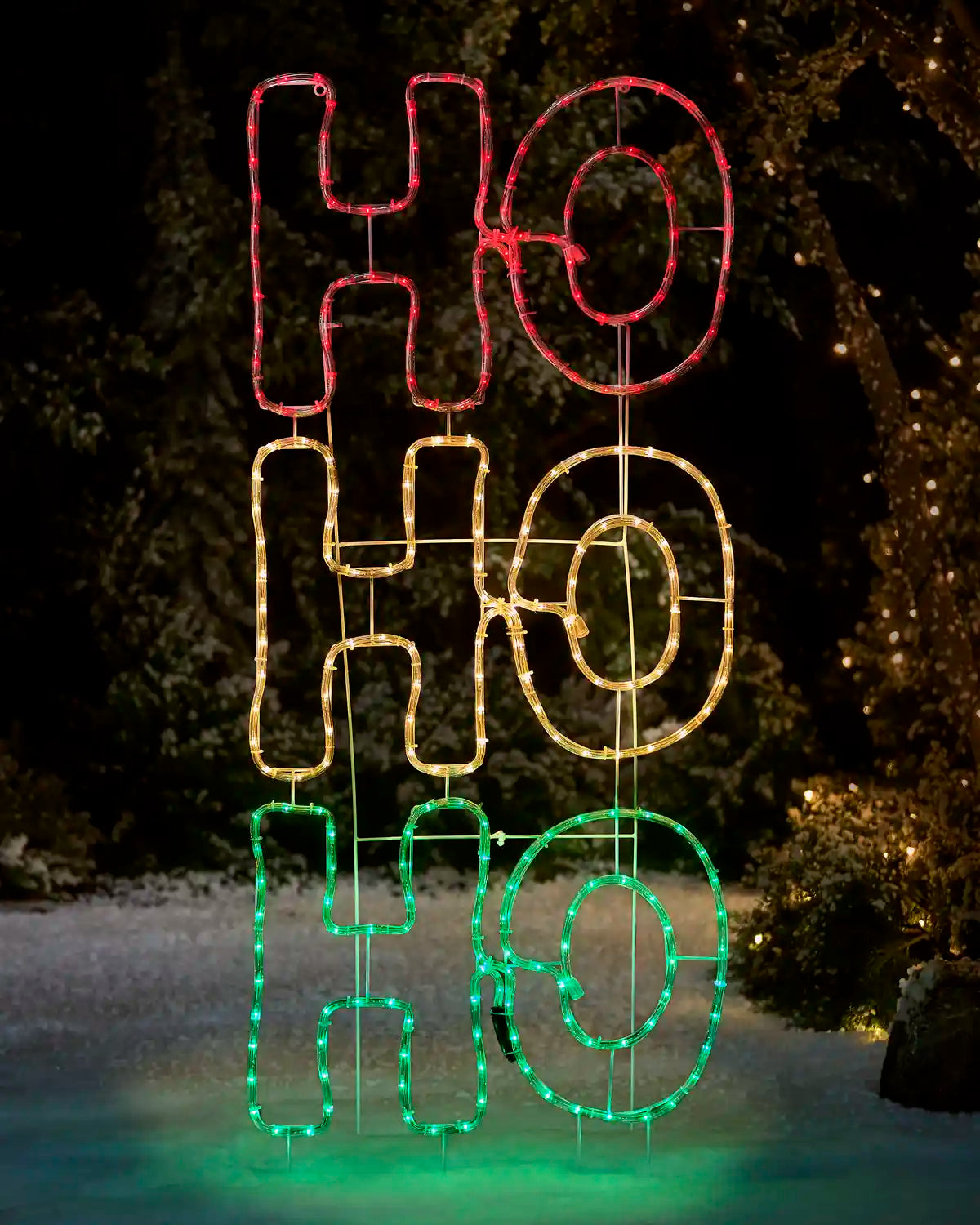 Three-dimensional rope light sign spelling 'HO HO HO' in red, gold, and green, lit up at night with a snowy outdoor background.
