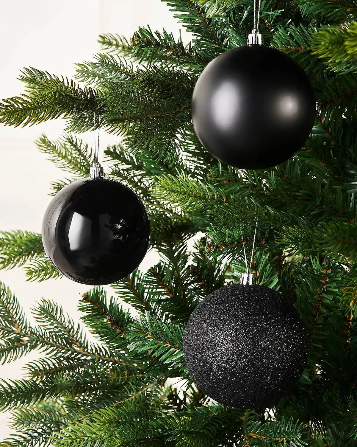 Three Black baubles hanging on a Christmas tree against a cream panel wall
