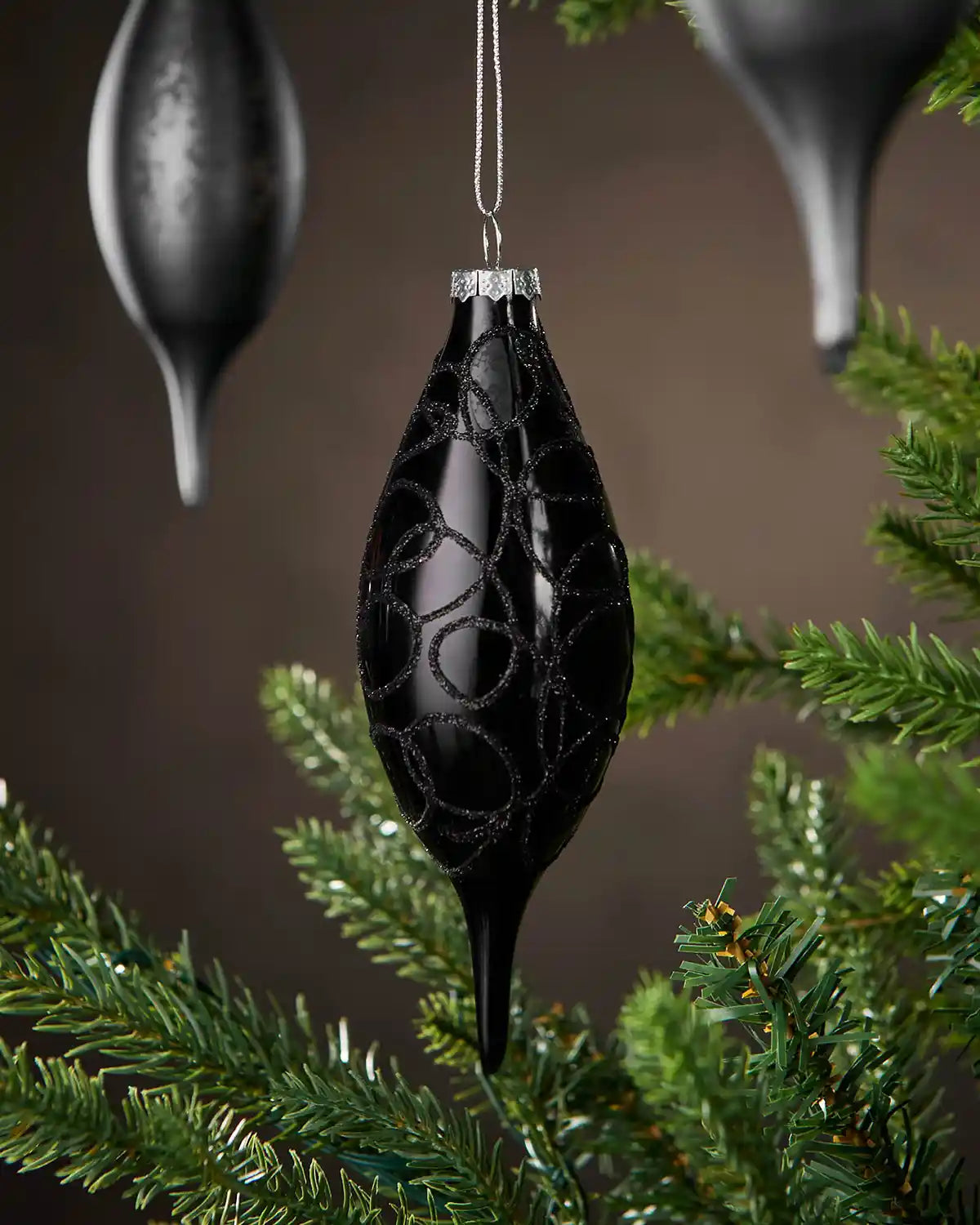 Three Black decorative ornaments with intricate patterns hanging on a Christmas tree.