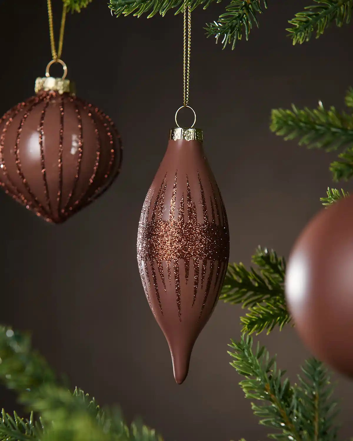 Three Decorative brown Christmas baubles hanging on a tree with a dark background