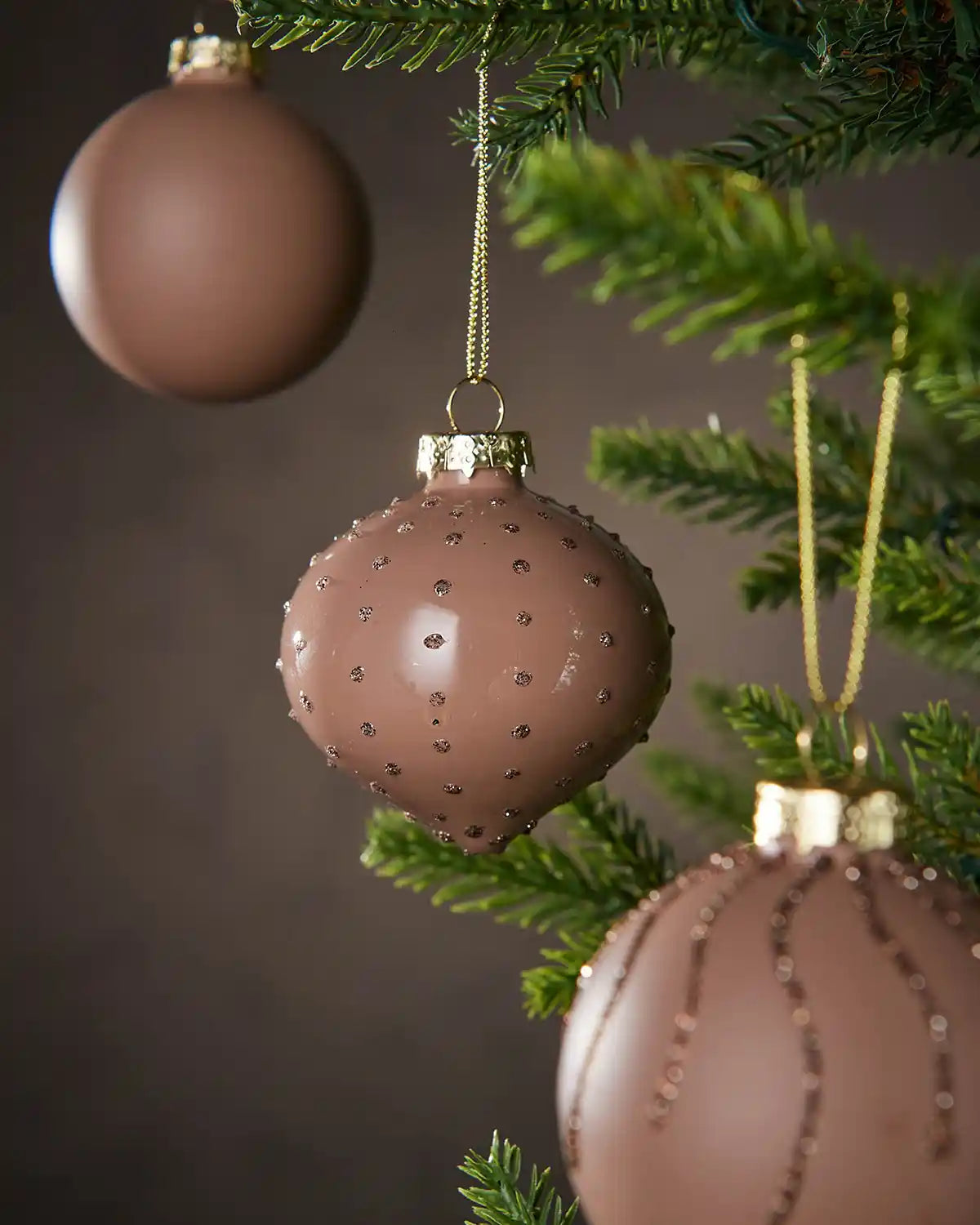 Three Decorative brown Christmas ornaments with gold accents hanging on a tree.
