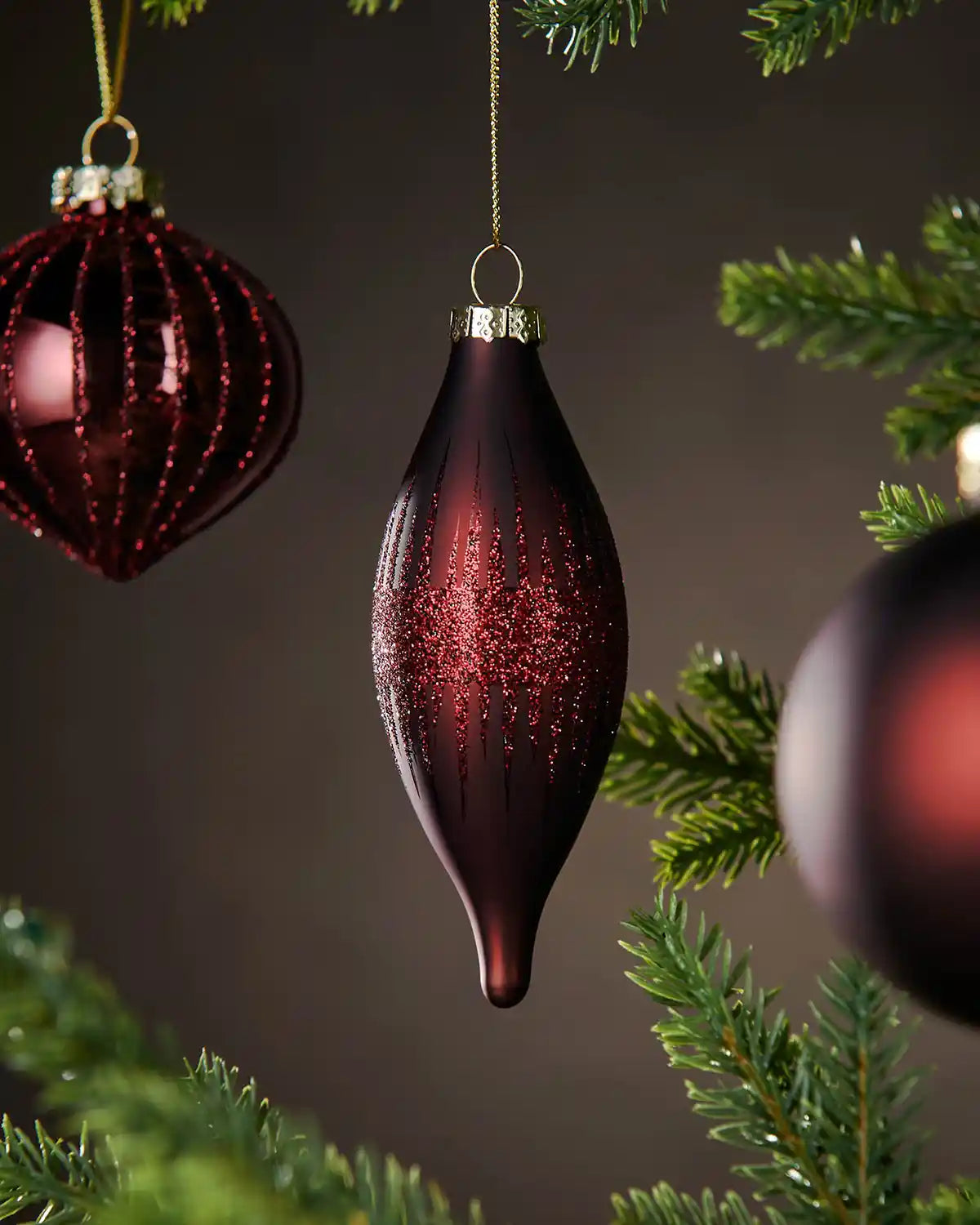 Three Decorative burgundy baubles hanging on a Christmas tree with a dark background
