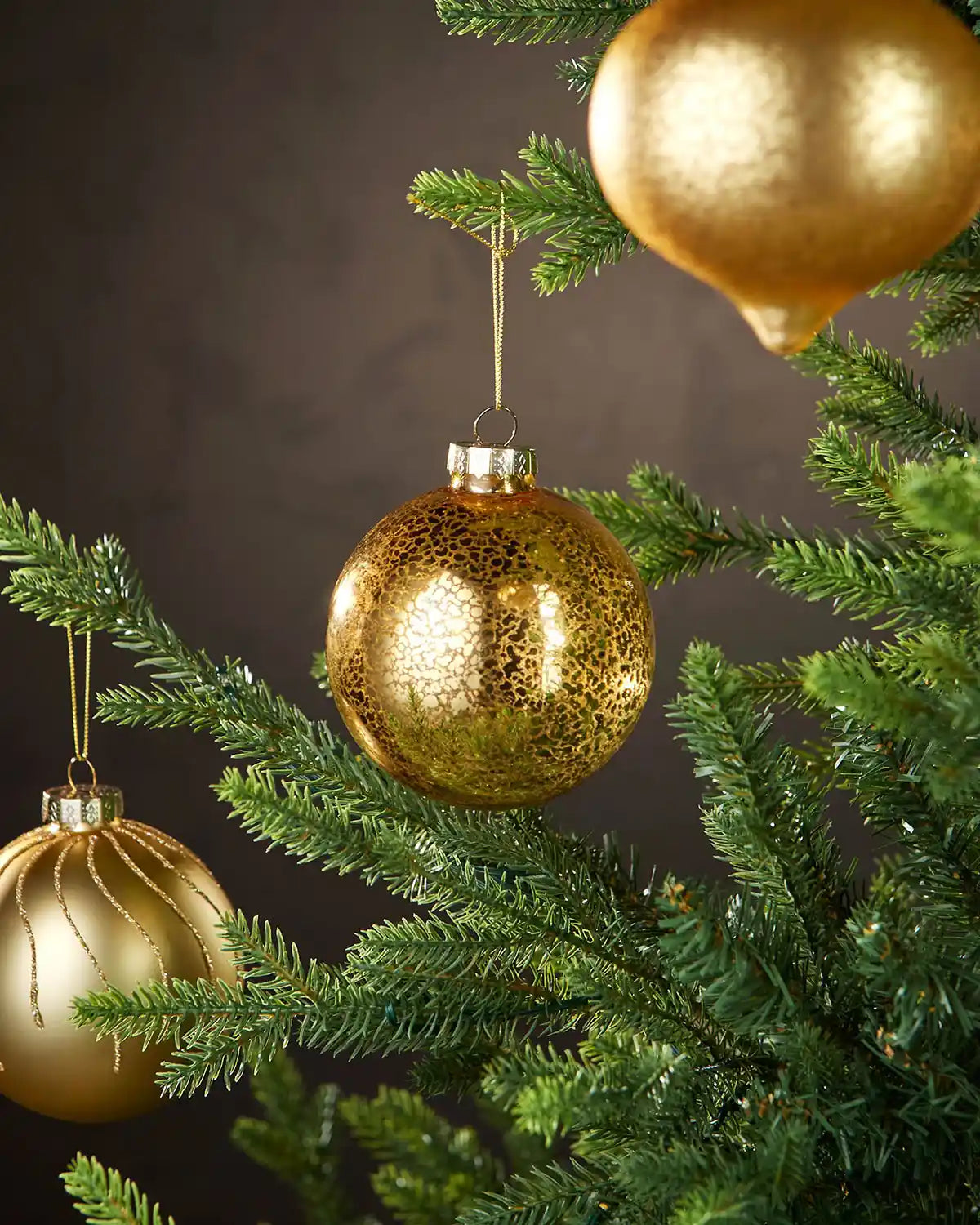 Three Gold Christmas baubles on a tree branch with a dark background