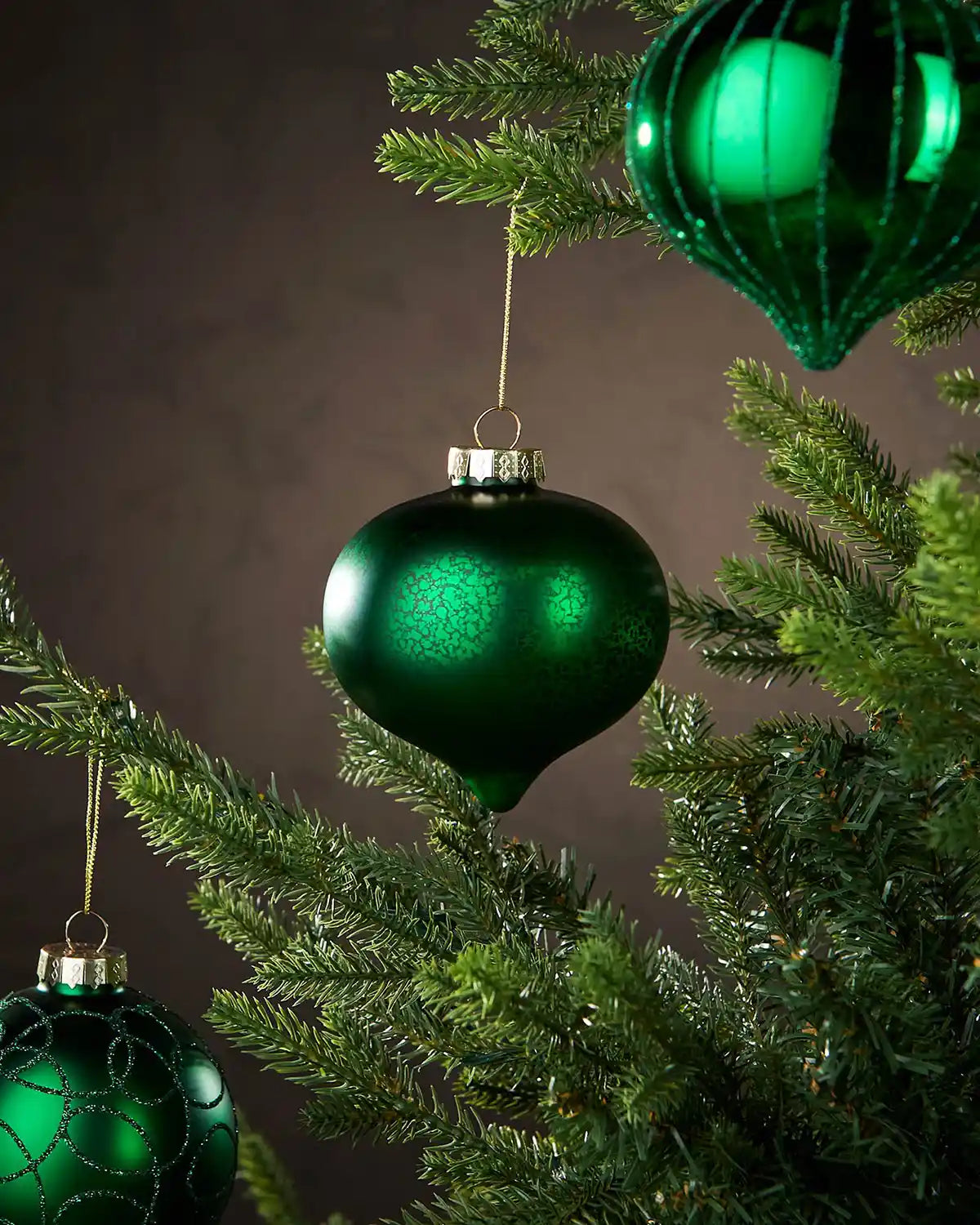 Three Green Christmas ornaments hanging on a tree with a dark background