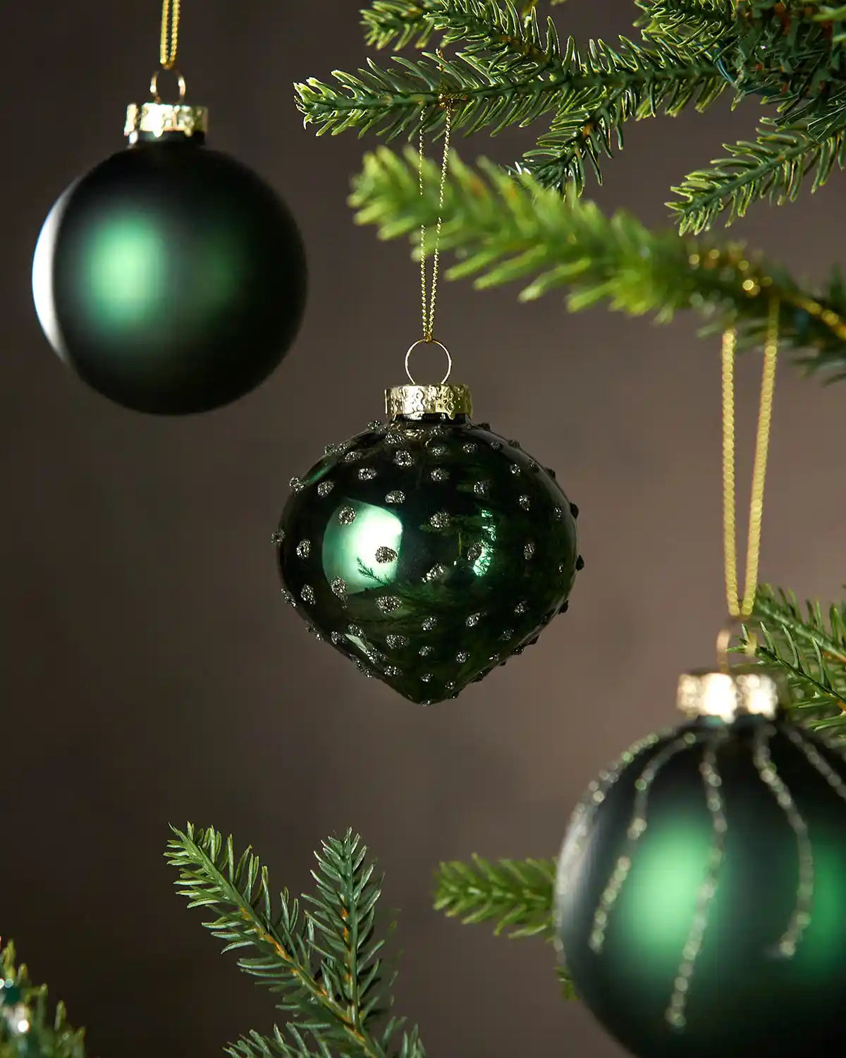 Three Green glass Christmas baubles hanging on a tree branch with a dark background