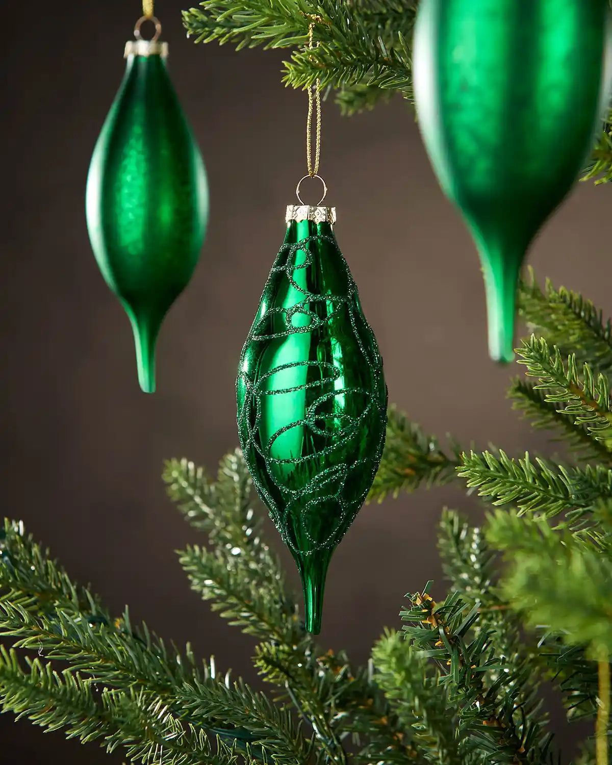 Three Green glass Christmas baubles in teardrop shapes hanging on a tree with a dark background