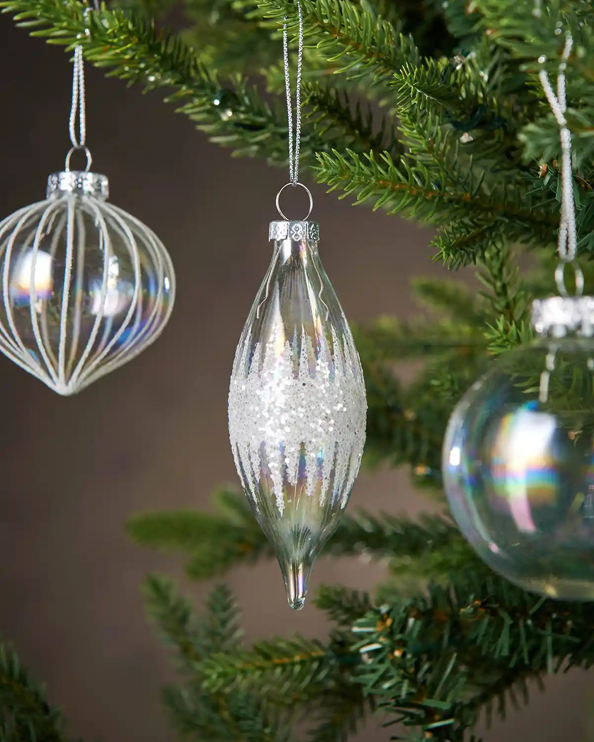Three Iridescent glass Christmas baubles hanging on a tree with a blurred background