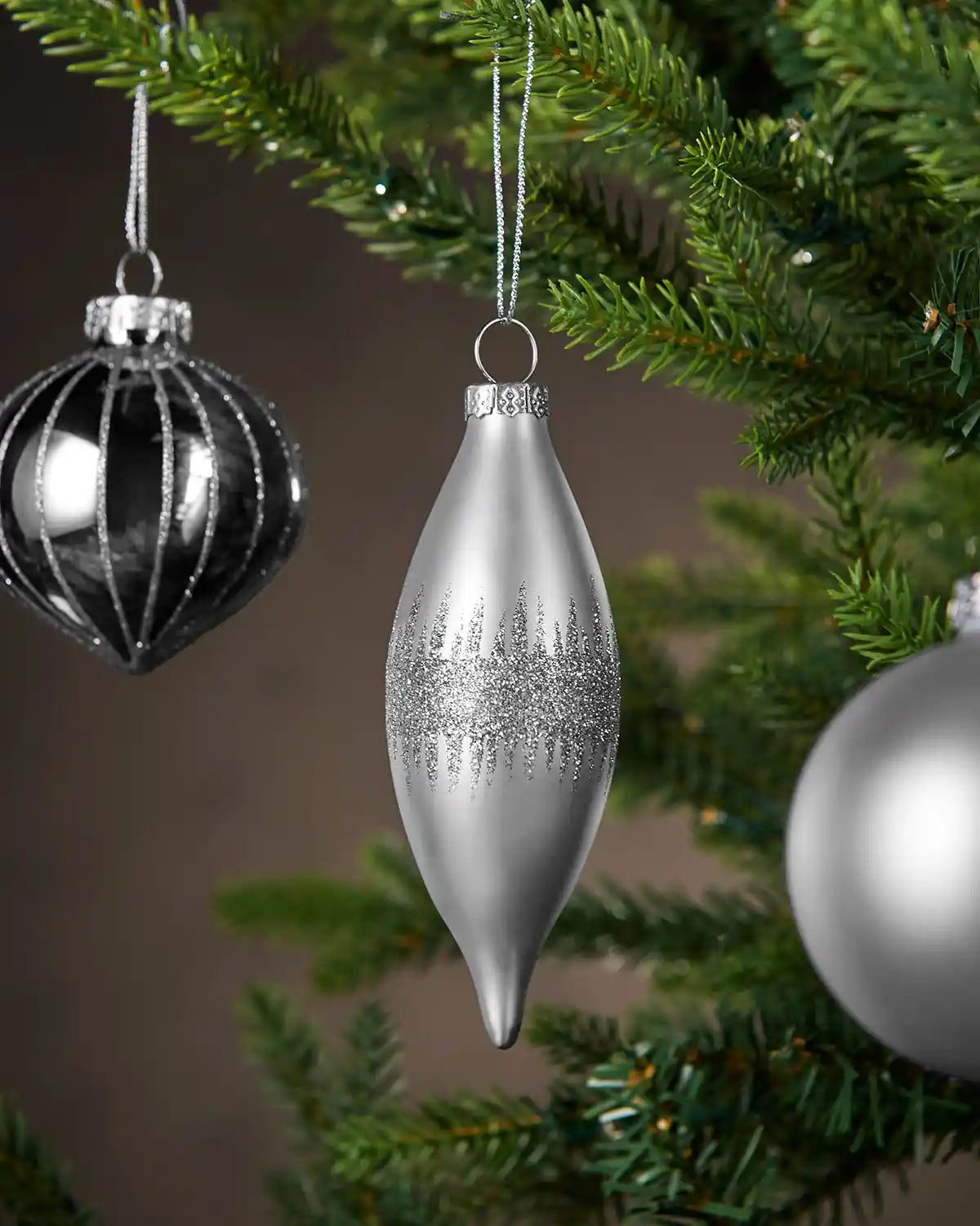 Three Silver Christmas baubles hanging on a tree branch with a blurred background