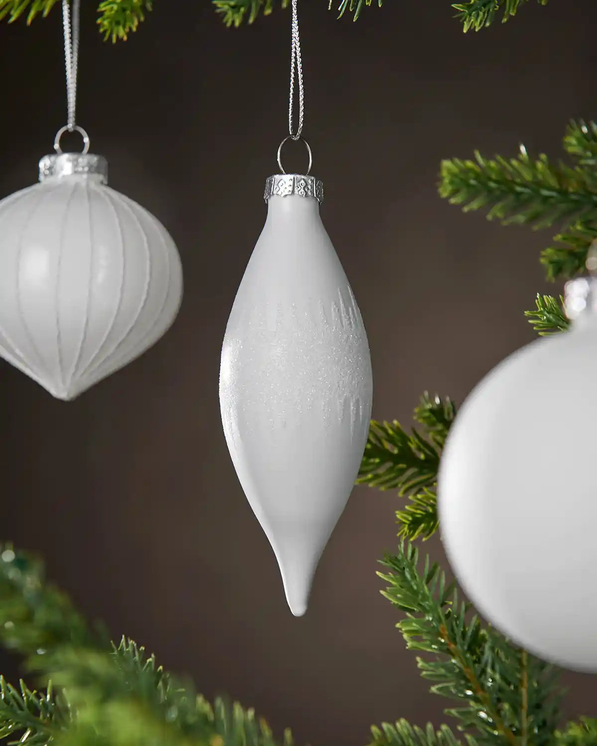 Three White glass Christmas baubles hanging on a tree branch with a dark background
