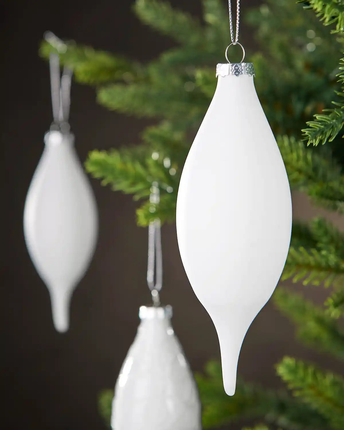 Three White teardrop-shaped baubles hanging on a Christmas tree.