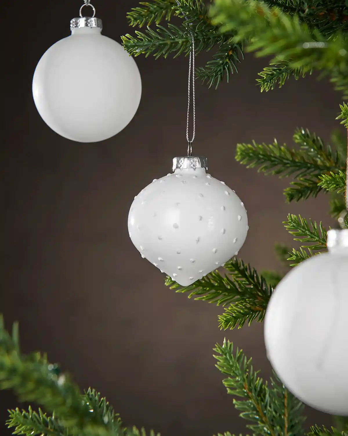 Three White textured Christmas Baubles hanging on a tree branch with a dark background