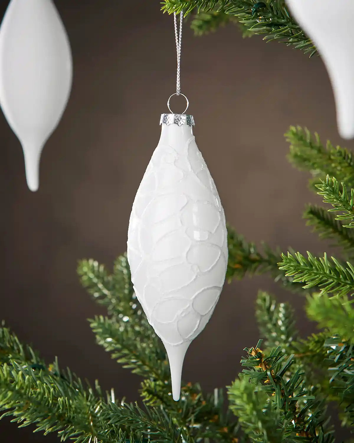 Three White textured Christmas ornament hanging on a tree branch with a brown background