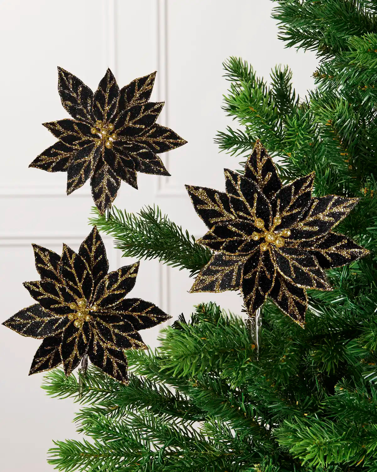 Three black glitter artificial poinsettias with gold glitter detailing displayed on a green Christmas tree