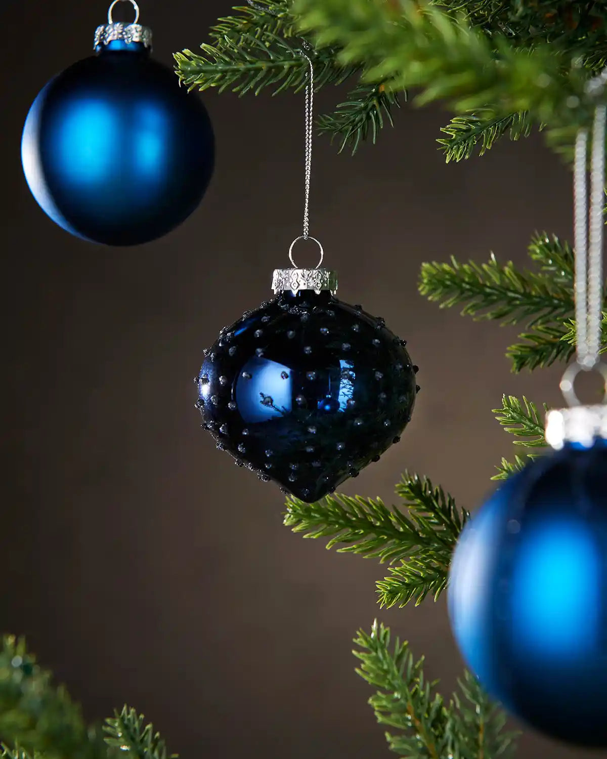 Three blue Christmas  baubles hanging on a tree with a dark background