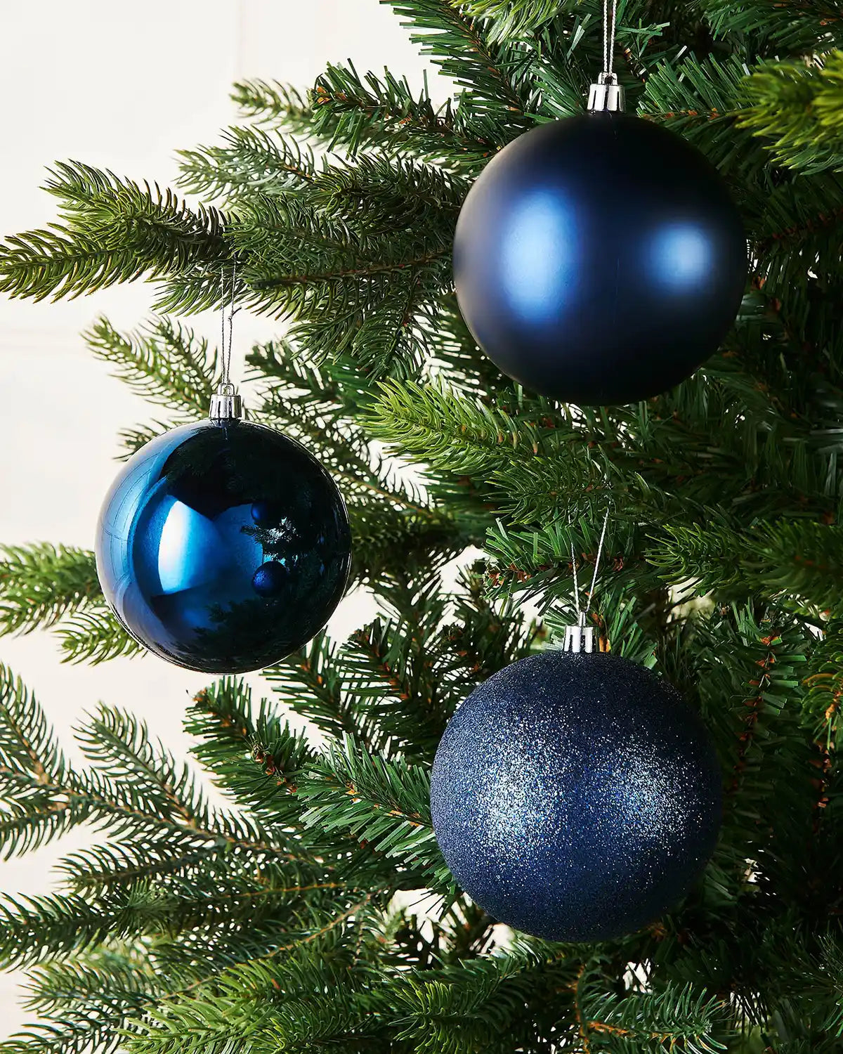 Three blue Christmas ornaments hanging on a green tree.