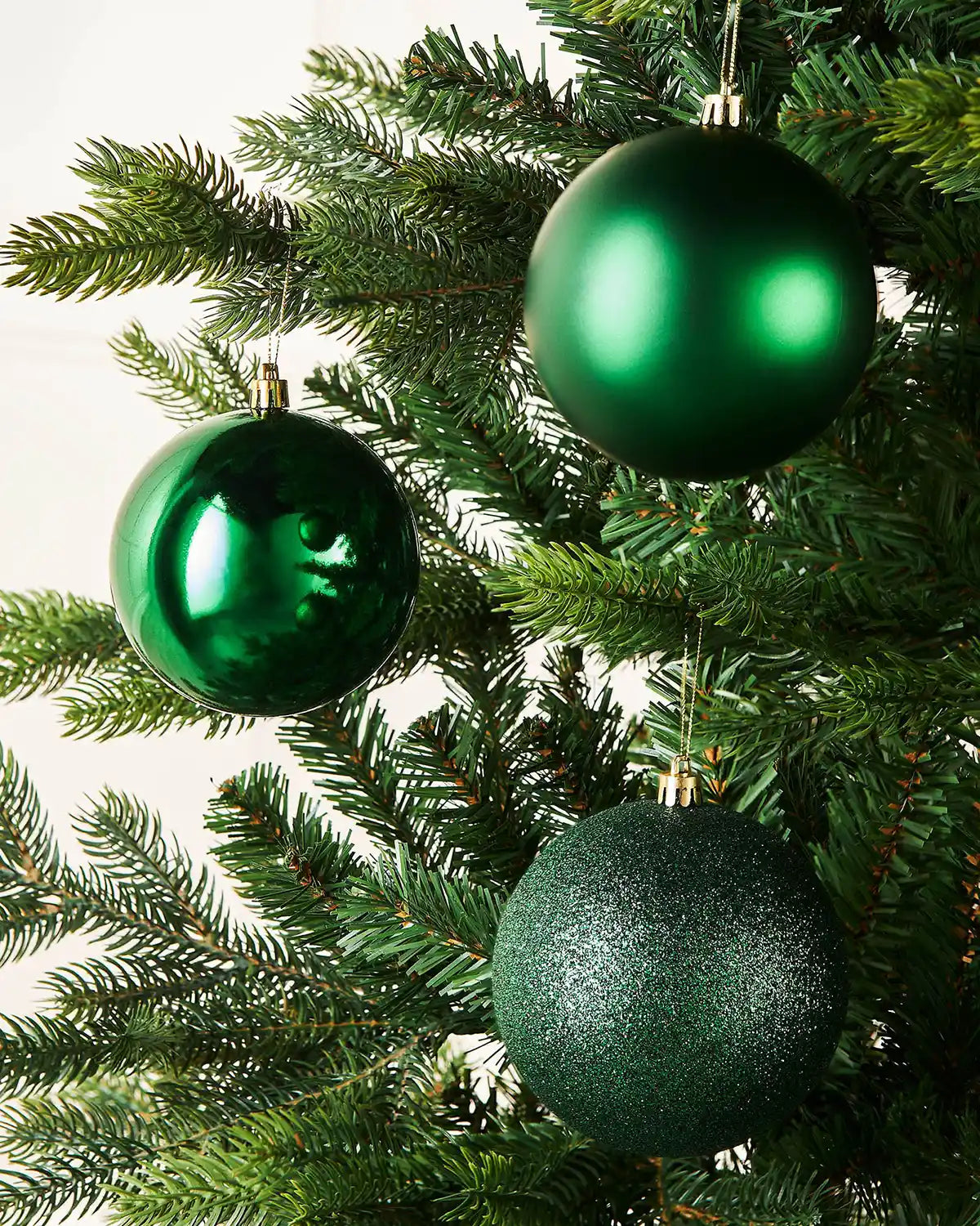 Three green Christmas baubles on a Christmas tree on a cream background