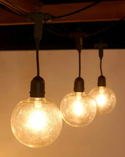 Three illuminated light bulbs hanging from a wooden beam on a ceiling fixture against a neutral background