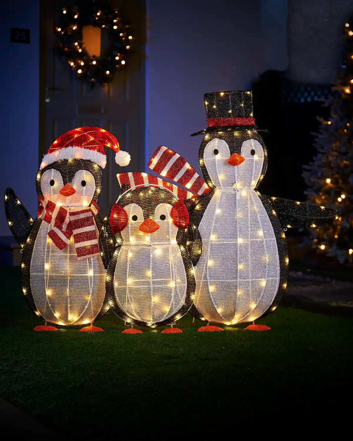 Three illuminated penguin decorations with festive hats and scarves on a dark background.
