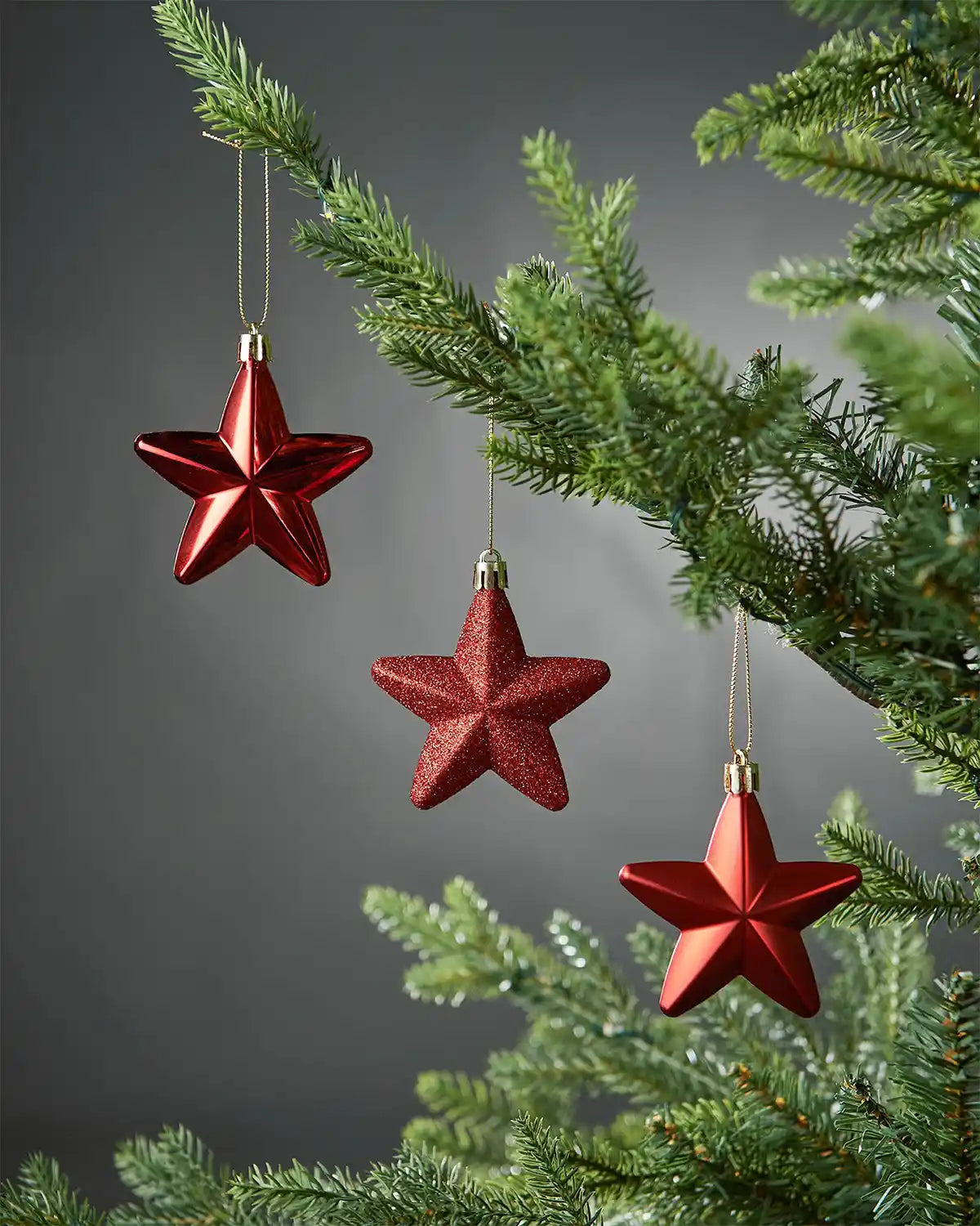 Three red star baubles with glitter, matt and glossy effects on a Christmas tree against a grey background 
