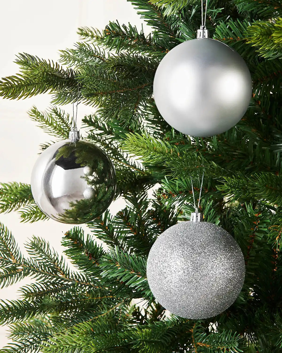 Three silver Christmas baubles on a Christmas tree against a cream wall