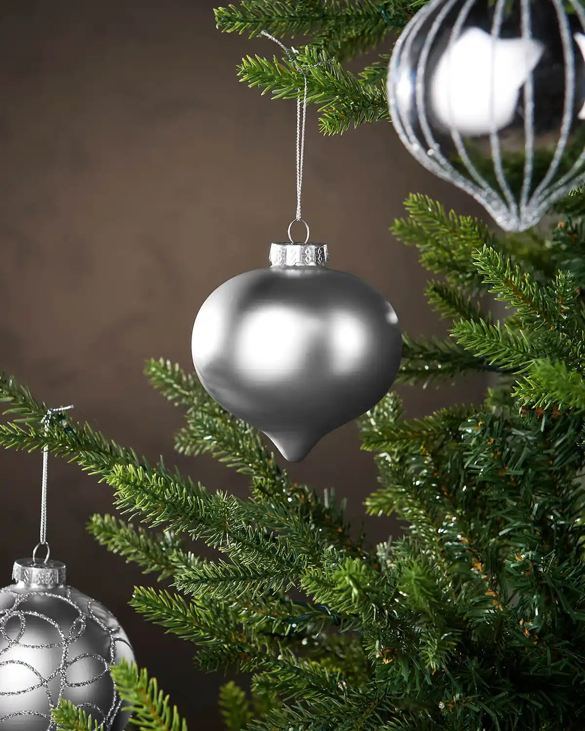 Three silver baubles hanging on a Christmas tree branch with a brown background 