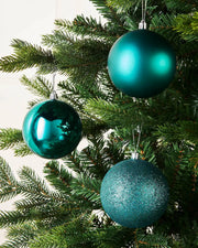 Three teal Christmas baubles on a tree branch against a cream wall