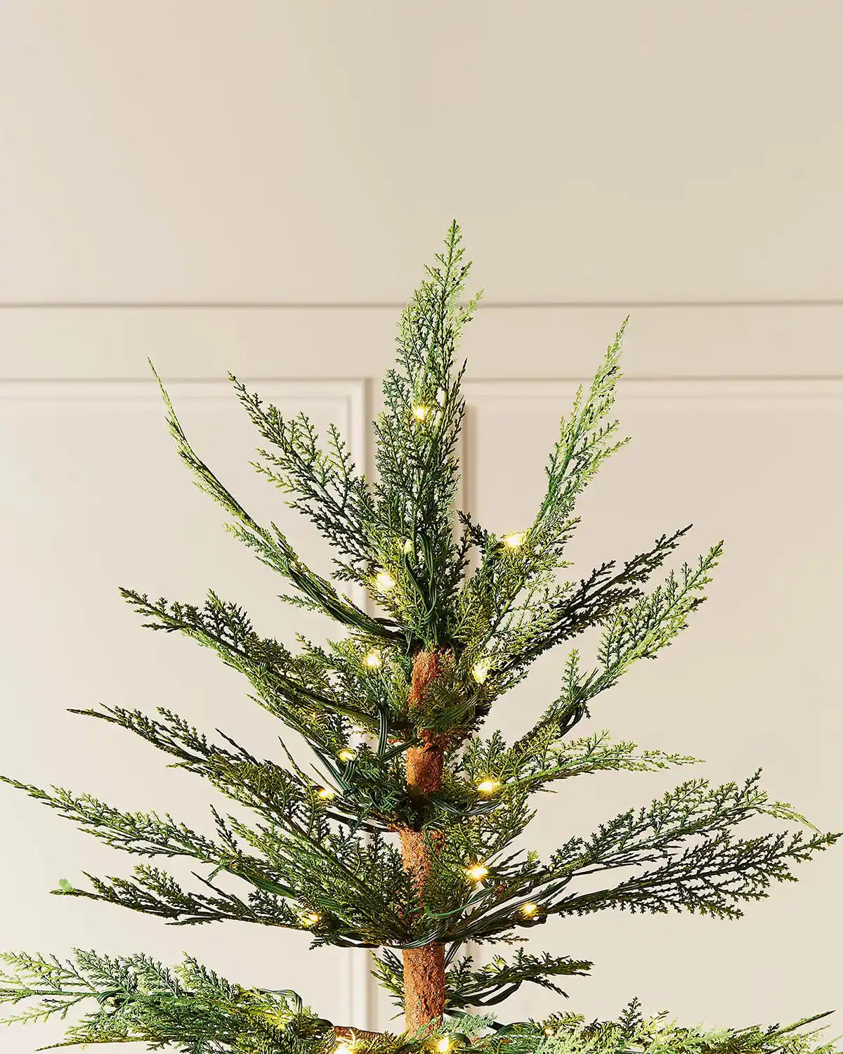 Top of 6.5ft pre-lit cypress pine Christmas tree with warm light setting in front of white panelling