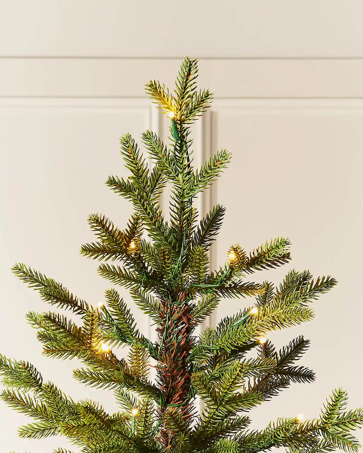 Close-up of top of 7ft pre-lit nordic pine Christmas tree with warm white light setting in front of white panelling
