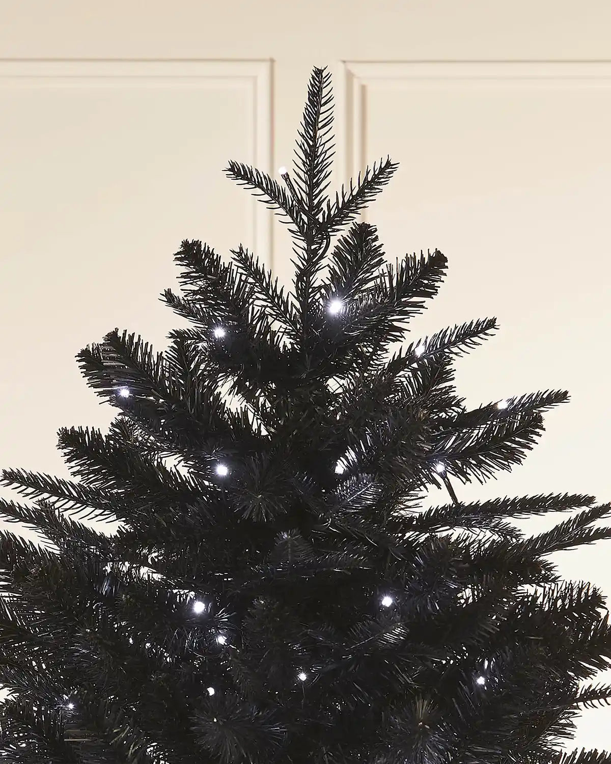 Top of 8ft pre-lit black pine Christmas tree with bright white light setting in front of white panelling