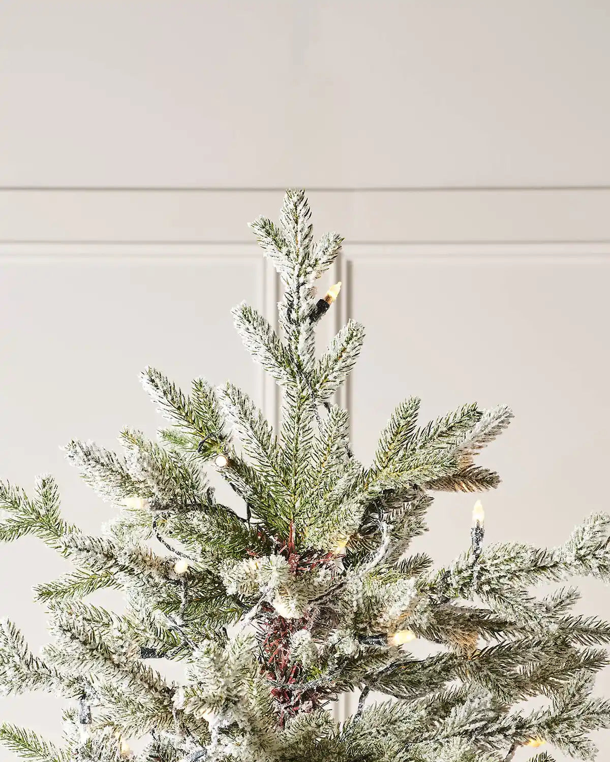 Top of 9ft Christmas tree with warm white lights against a neutral wall