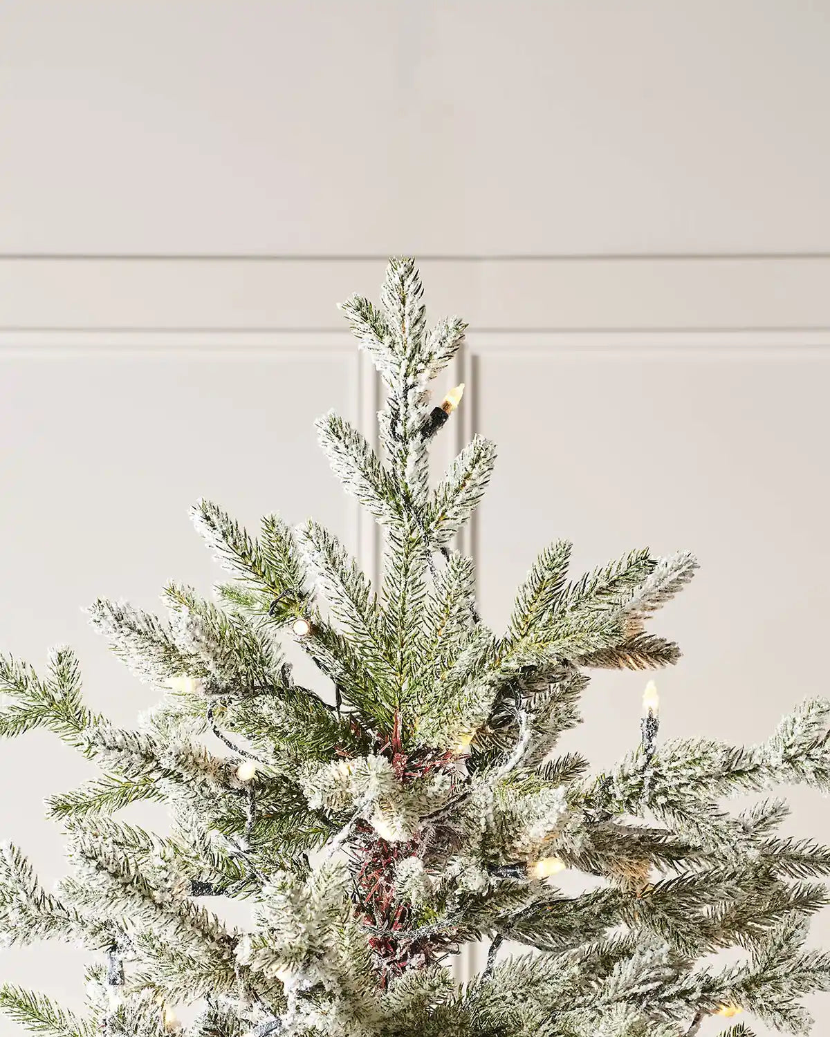 Top of Christmas tree with warm white lights against a neutral wall