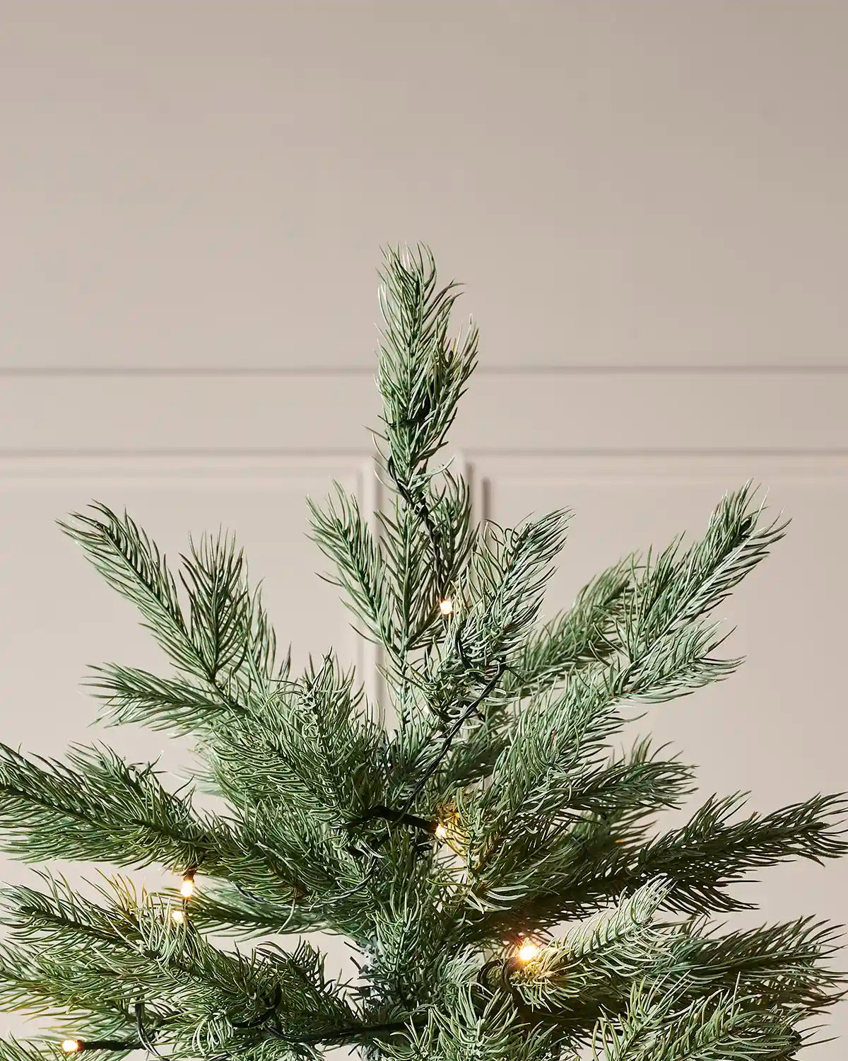 Top of green Artificial Christmas tree with lights against a neutral background