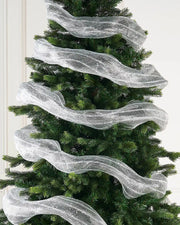 Transparent and silver foil mesh fabric ribbon wrapped around Christmas tree against a cream panel wall