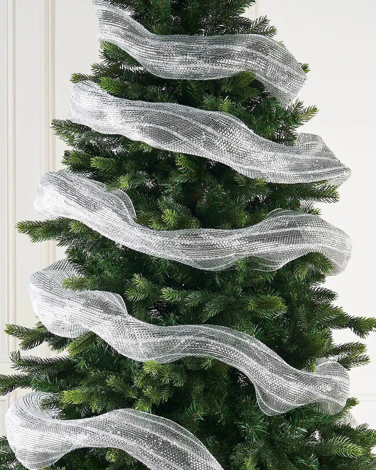 Transparent and silver foil mesh fabric ribbon wrapped around Christmas tree against a cream panel wall