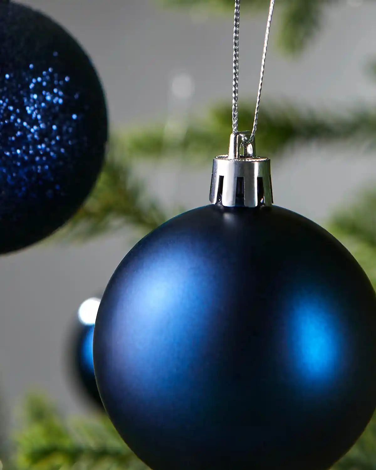 Two Blue Christmas baubles with silver cap on a blurred green background