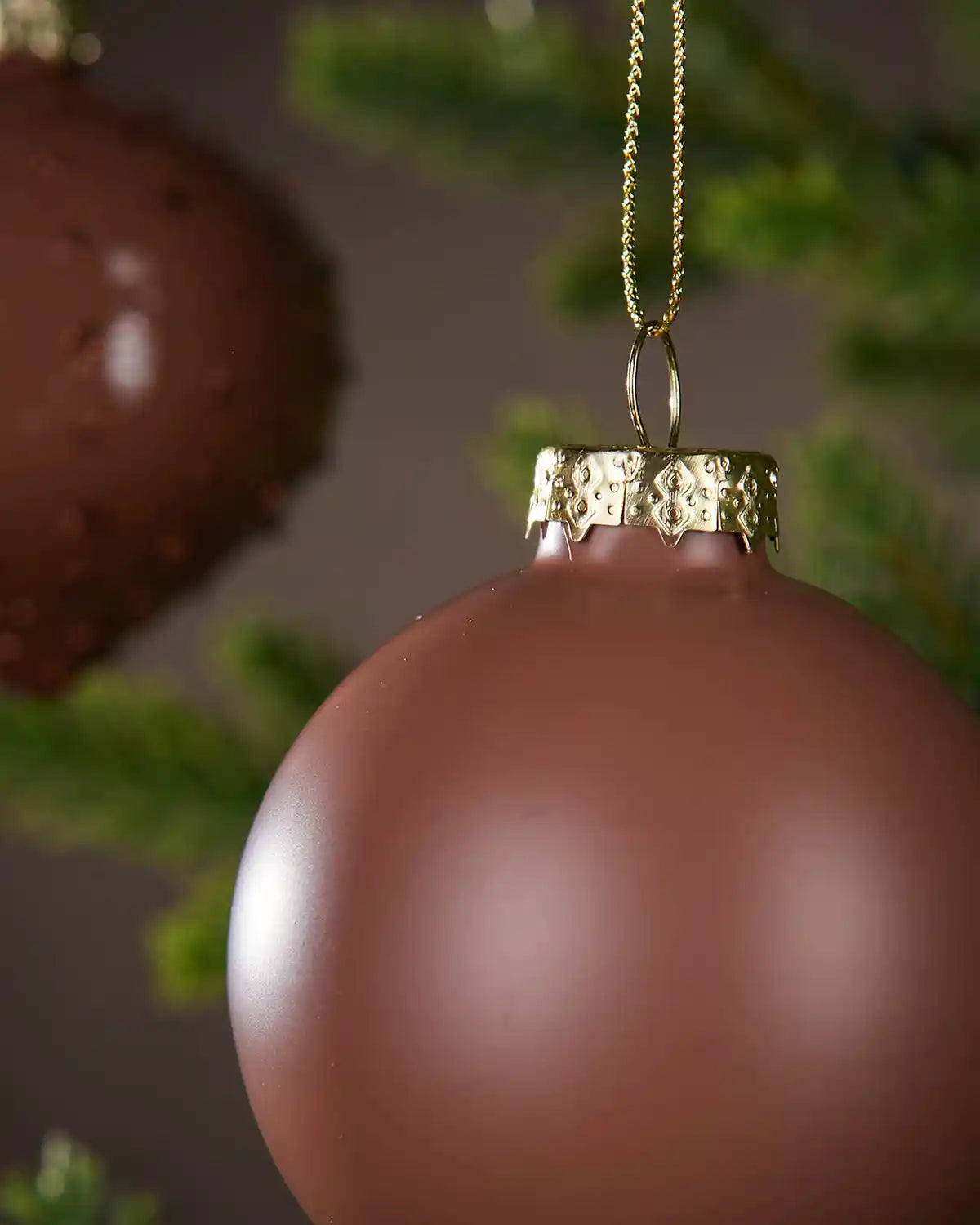 Two Brown Christmas ornament with gold chain on a blurred green background