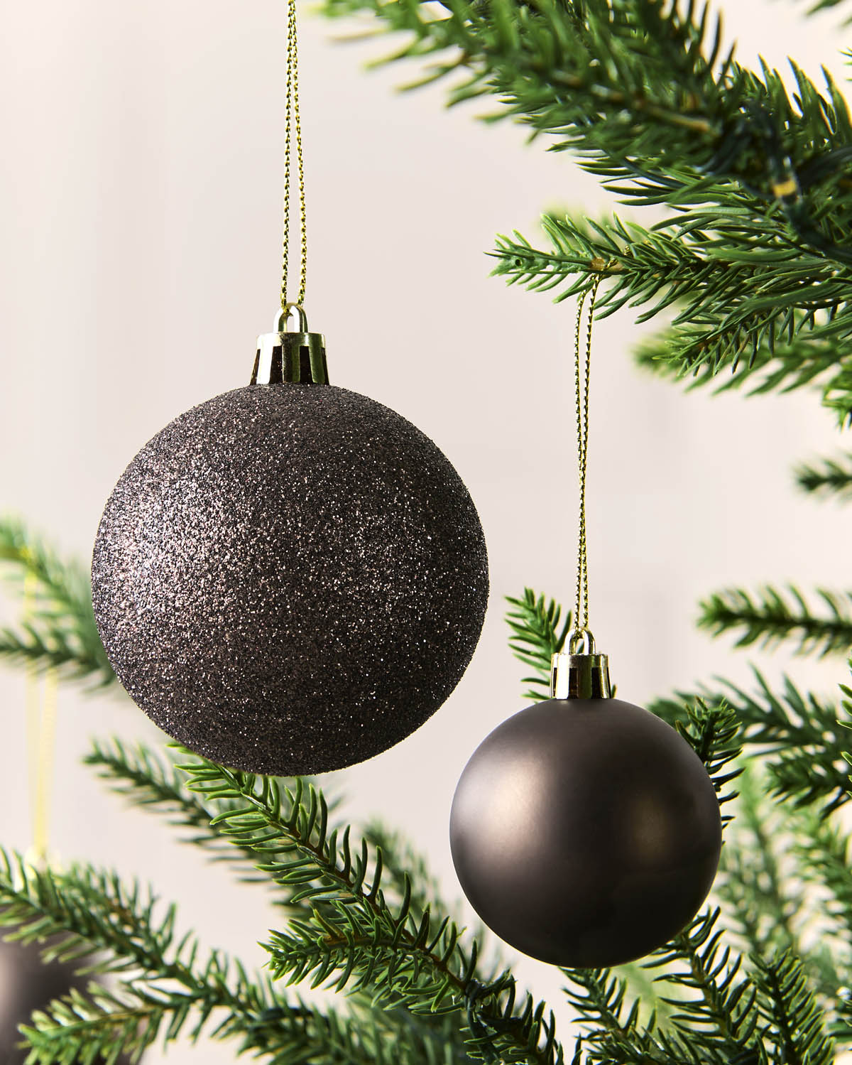 Two Mocha Christmas tree ornaments hanging from gold strings among green pine branches against a soft light background.