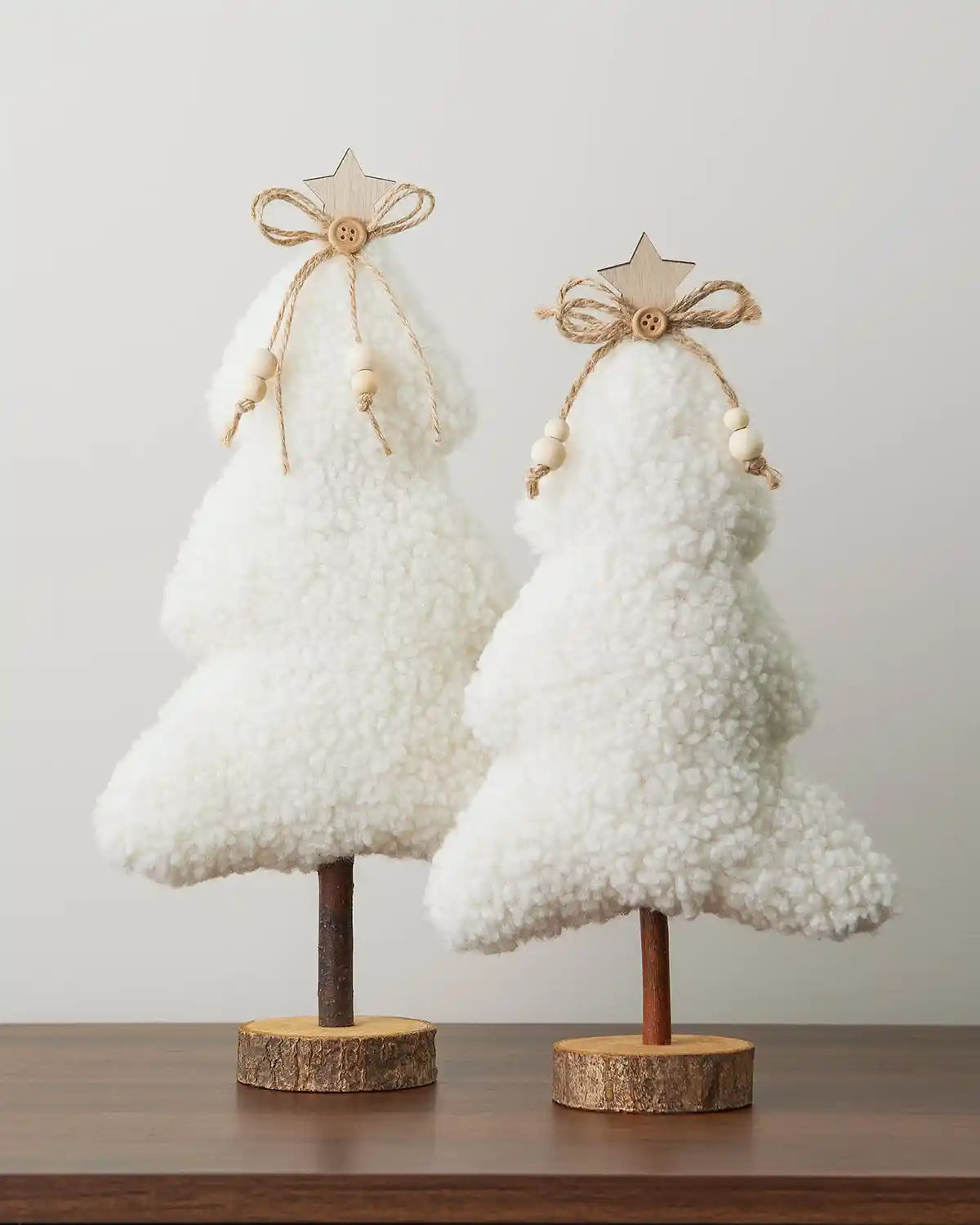 Two Sherpa mini trees with a wooden base on a table against a white wall