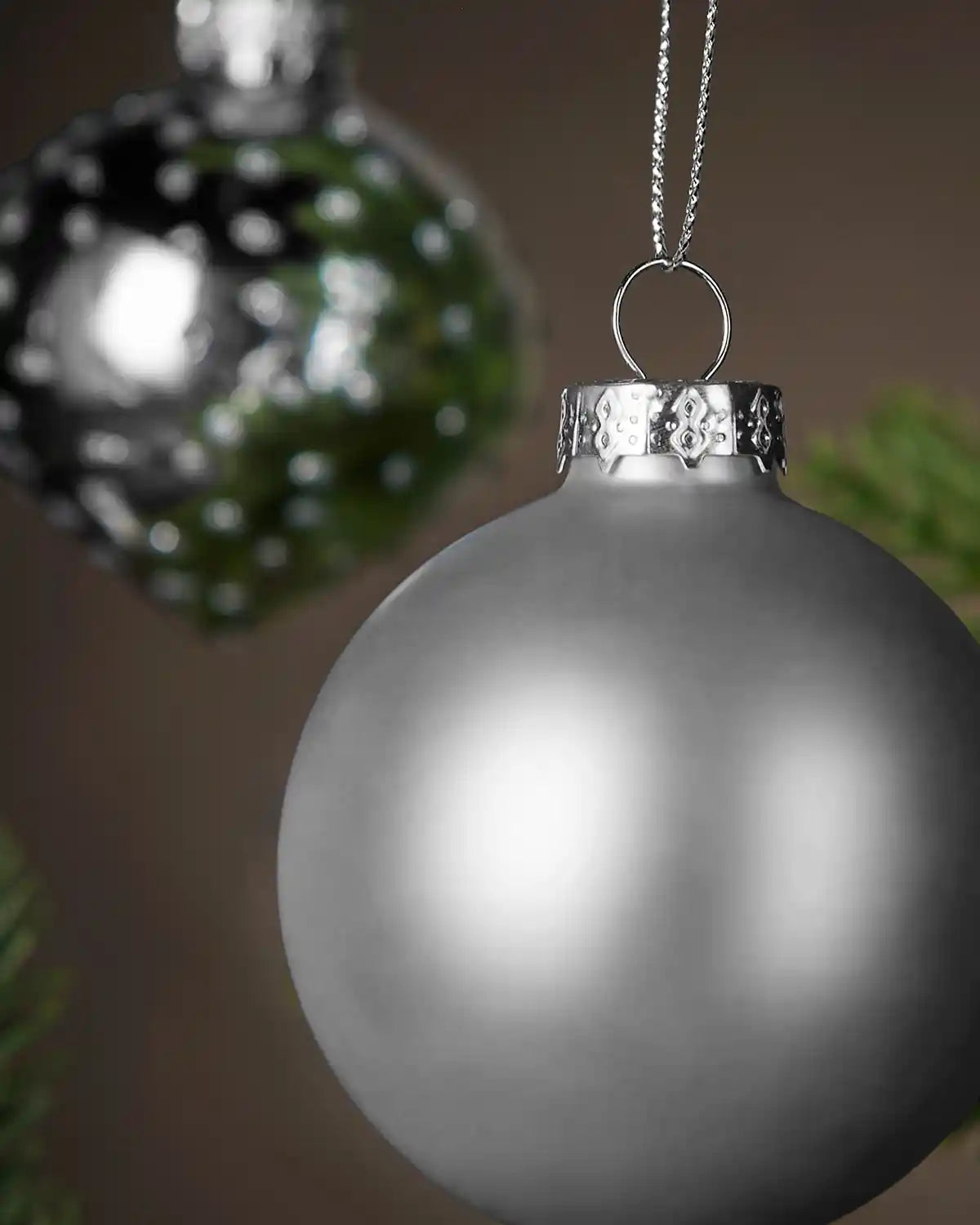 Two Silver Christmas ornament with a decorative cap on a blurred green background