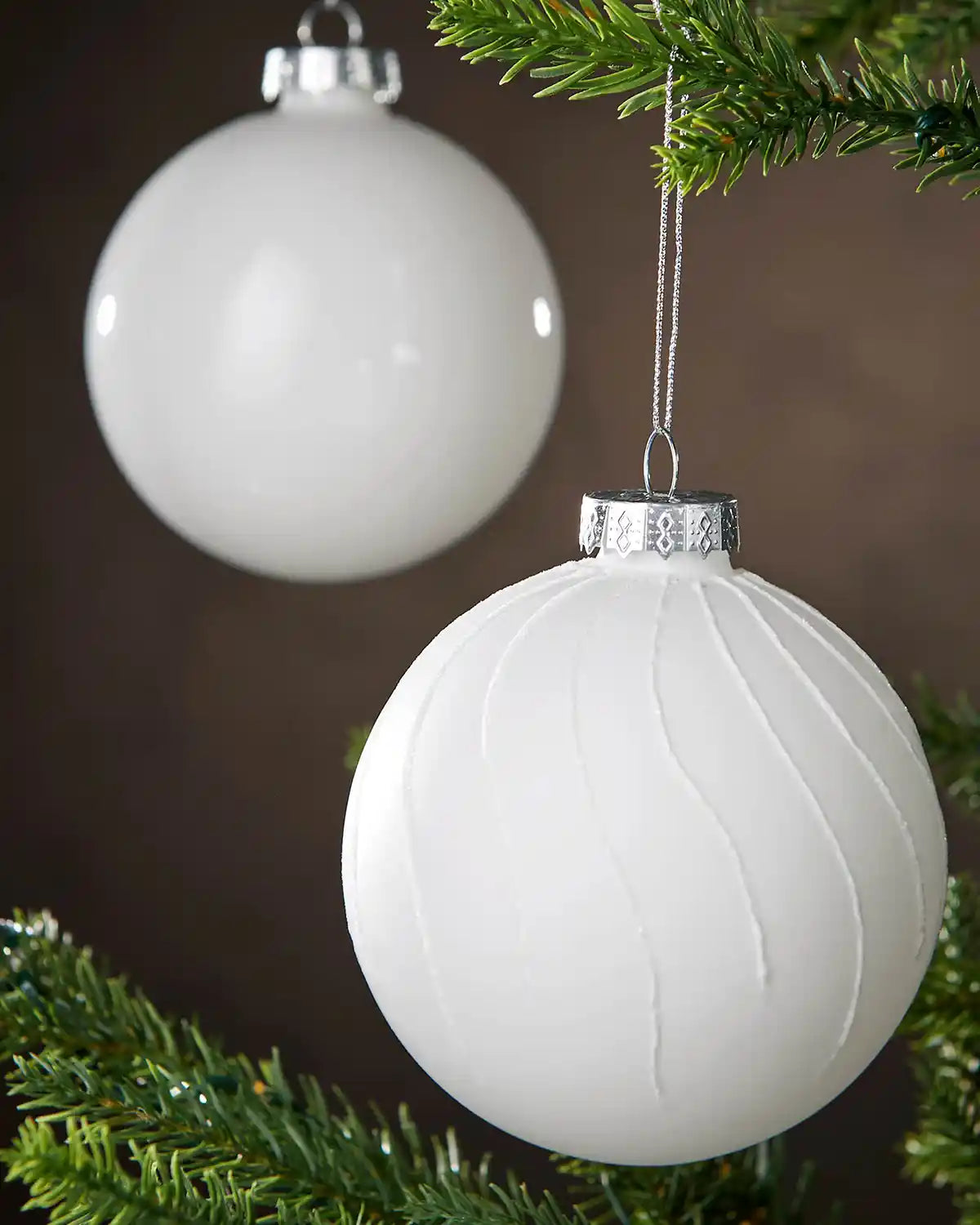 Two White Christmas ornaments hanging on a tree branch with a blurred background