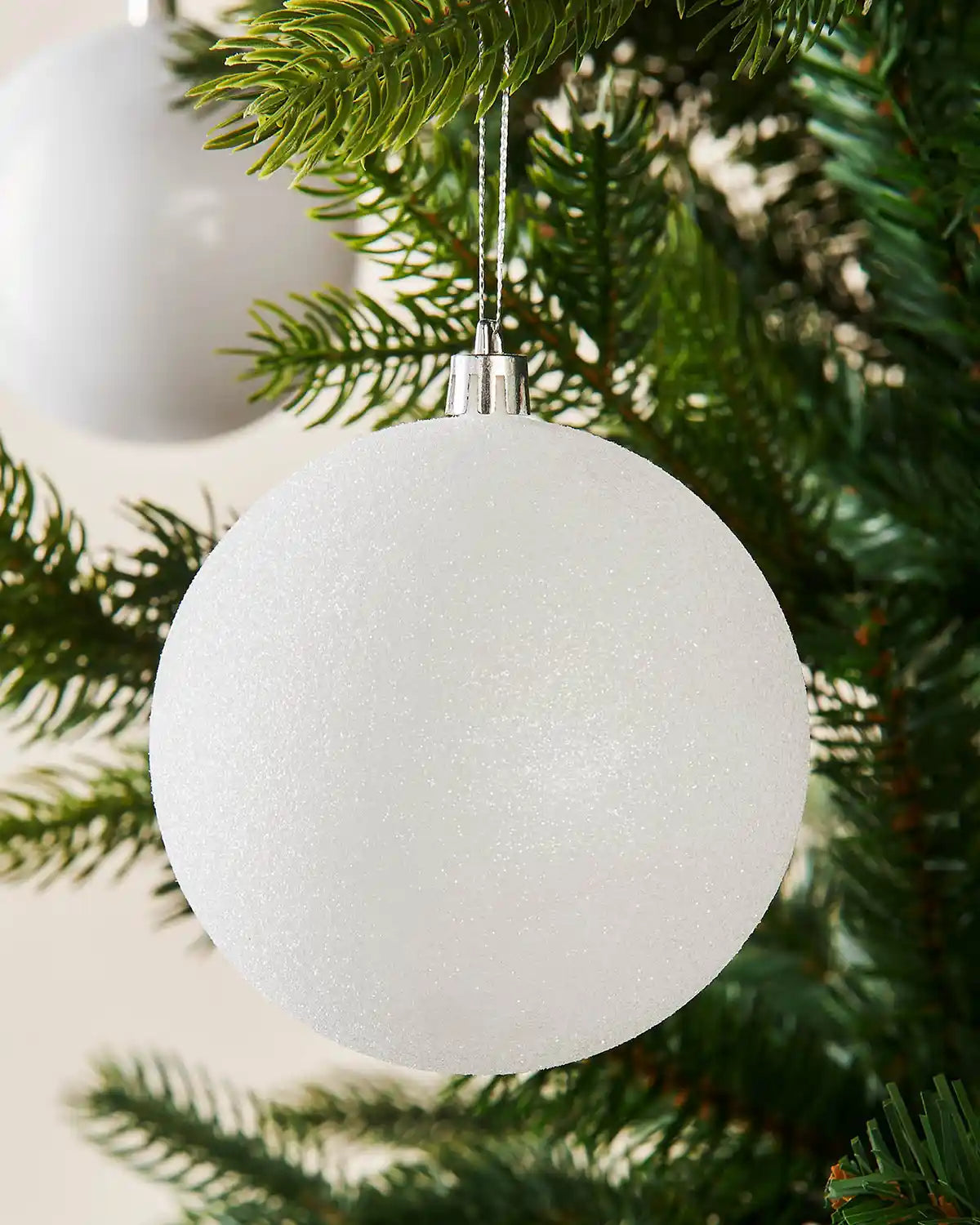 Two White glitter ornament hanging on a Christmas tree