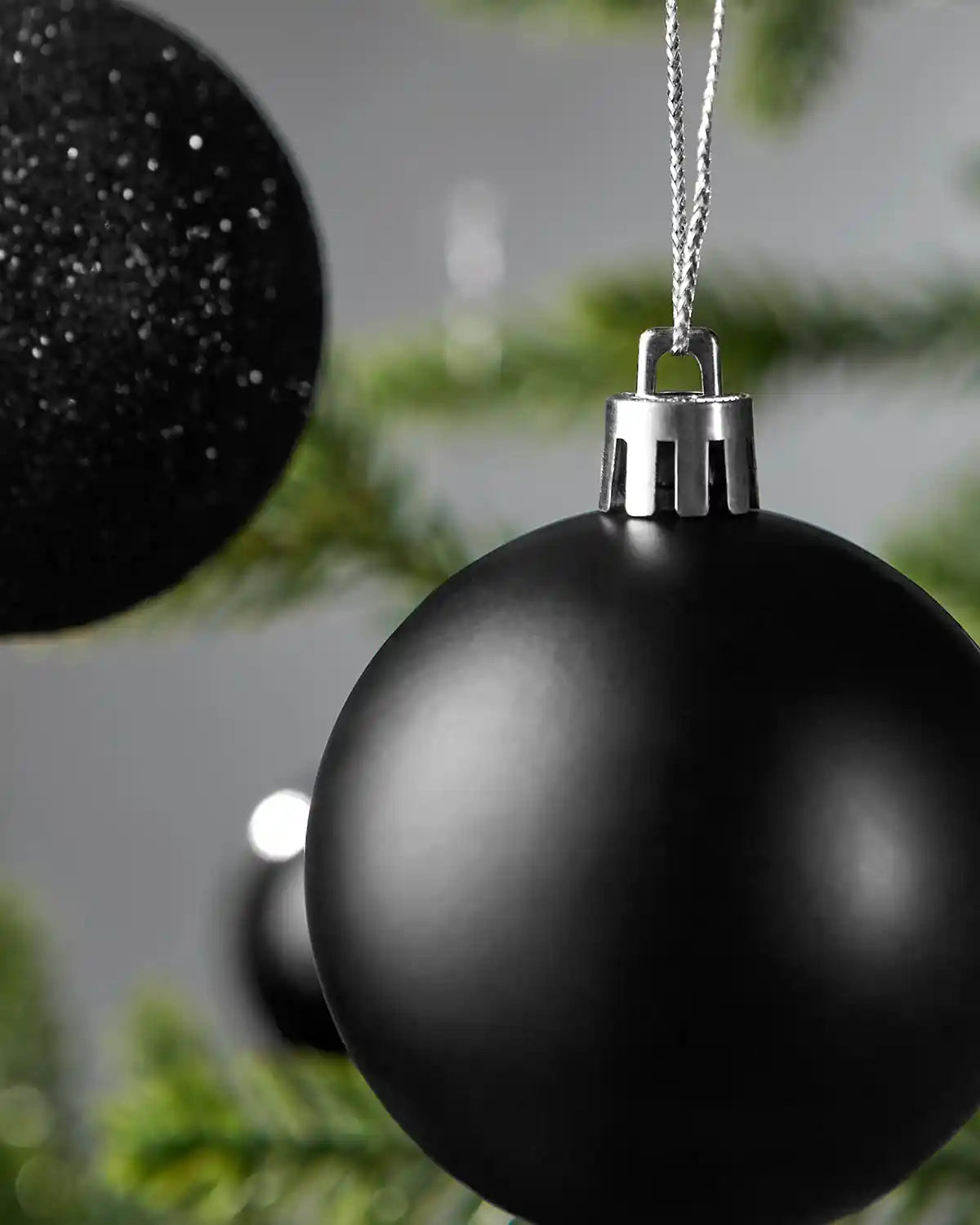 Two close up black Christmas baubles hanging on a tree branch with a grey background