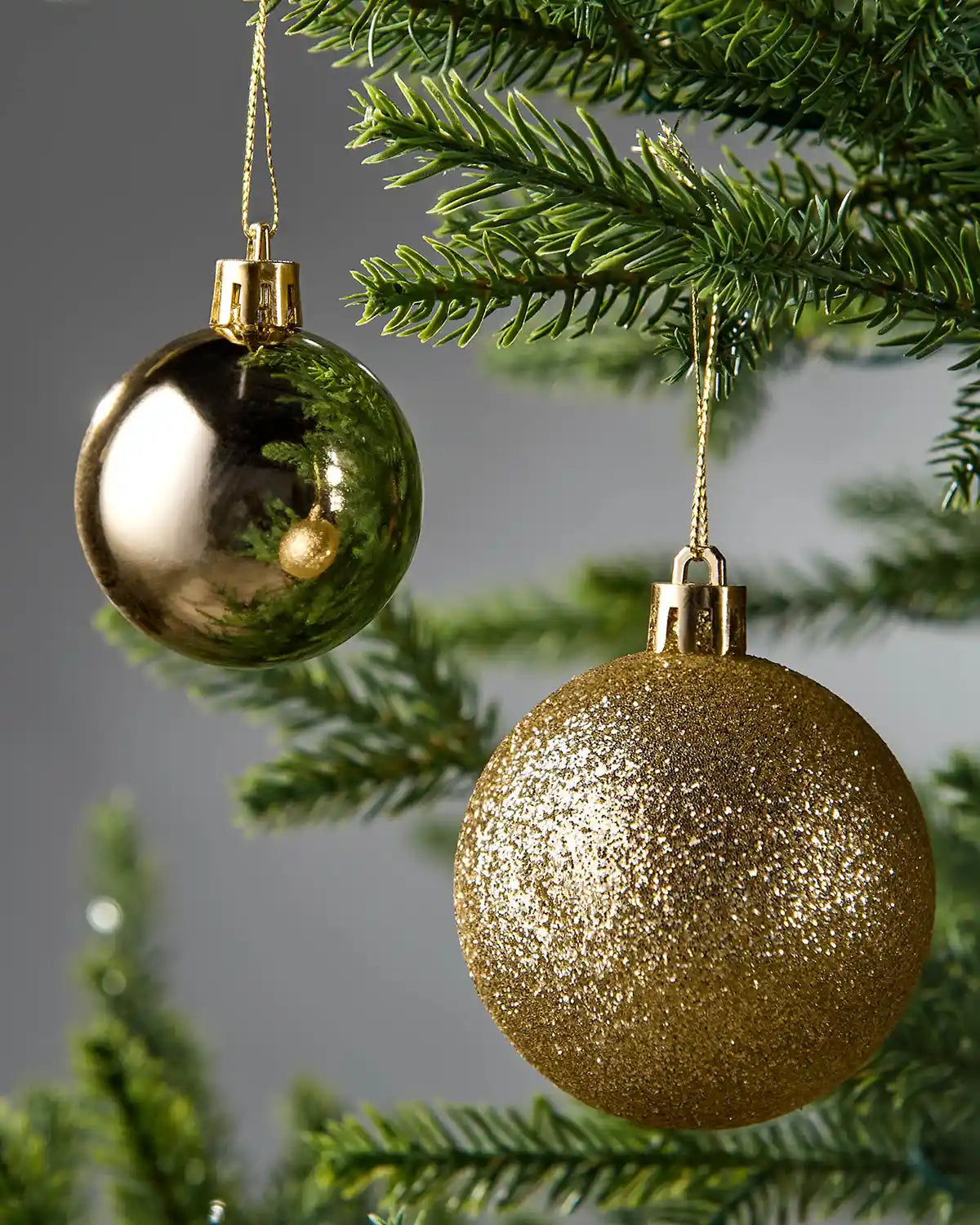 Two gold Christmas baubles hanging on a tree branch with a blurred grey background