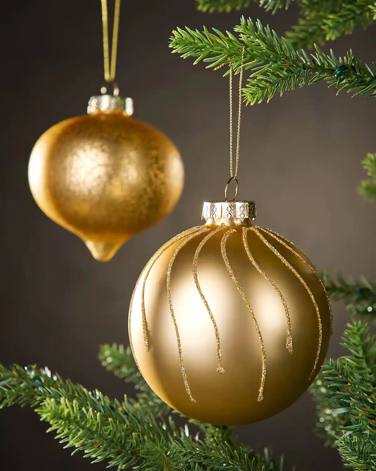 Two gold Christmas baubles hanging on a tree branch with a dark background