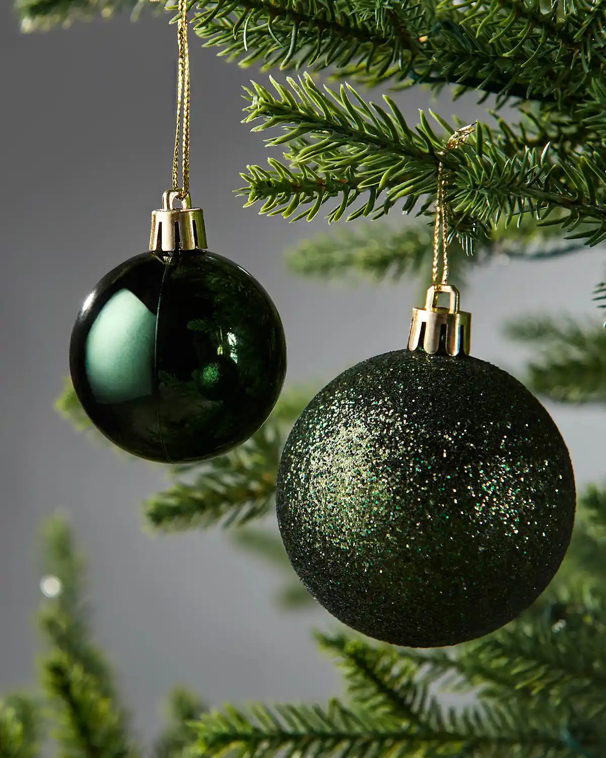 Two green Christmas baubles hanging on a tree branch with a blurred background