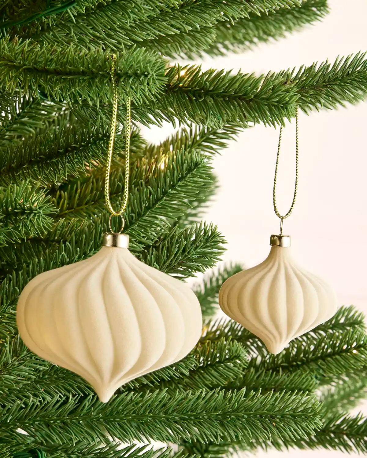 Two latte-coloured velvet baubles with ribbed detailing hanging from green Christmas tree branches
