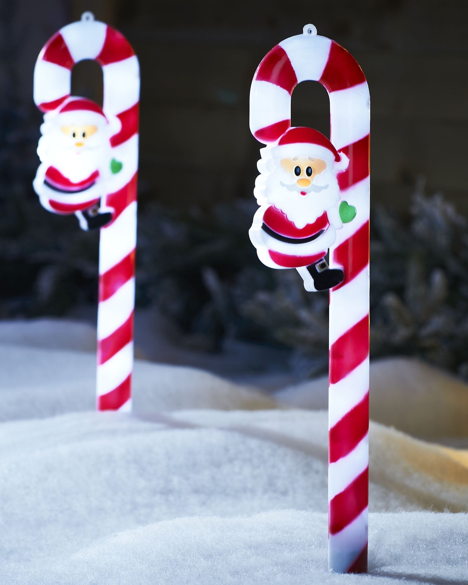 Two red and white Santa Claus candy cane garden stakes on a snowy garden background 