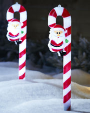 Two red and white Santa Claus candy cane garden stakes on a snowy garden background 