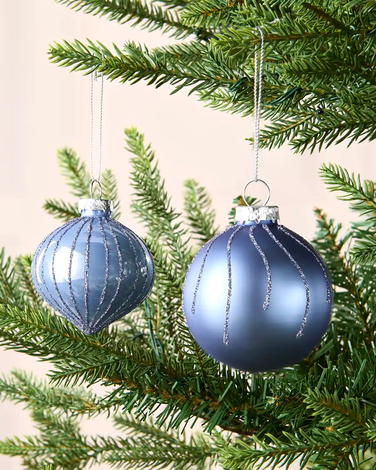 Two round Ice blue hanging baubles on a Christmas tree branch against a cream wall 