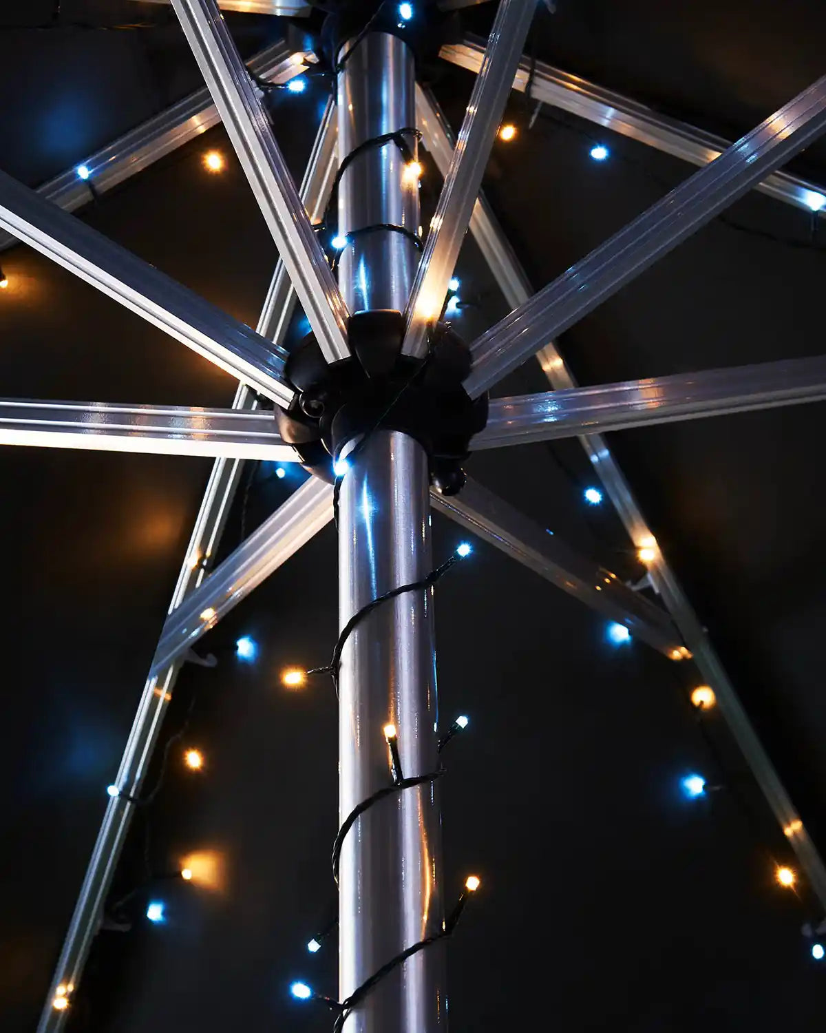 Umbrella pole with warm white and ice white string lights against a dark background